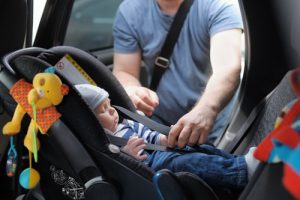 father fastening child in car seat